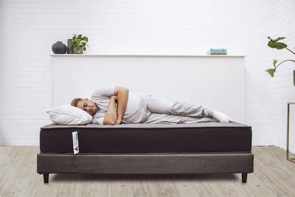 Man sleeping on side on Sleep Firm mattress in modern bedroom with white walls and wooden floor