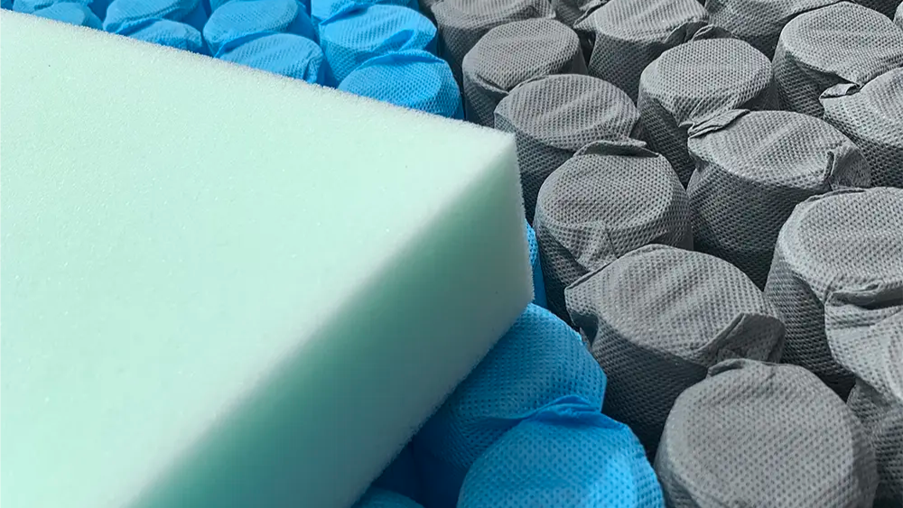 Close-up of blue and gray pocketed mattress springs with a light green foam layer on top