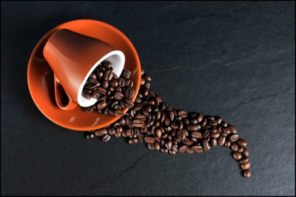 A mug on a saucer turned on its side, filled with coffee beans spilling onto the table. 